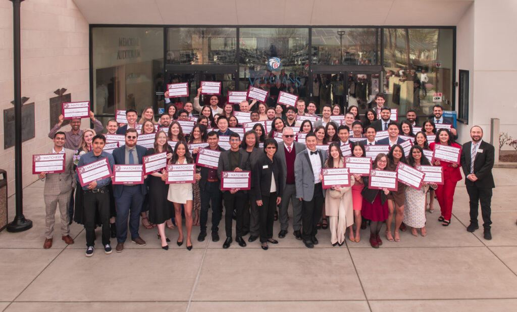 Group photo of students holding I Matched signs with faculty and staff in front of building