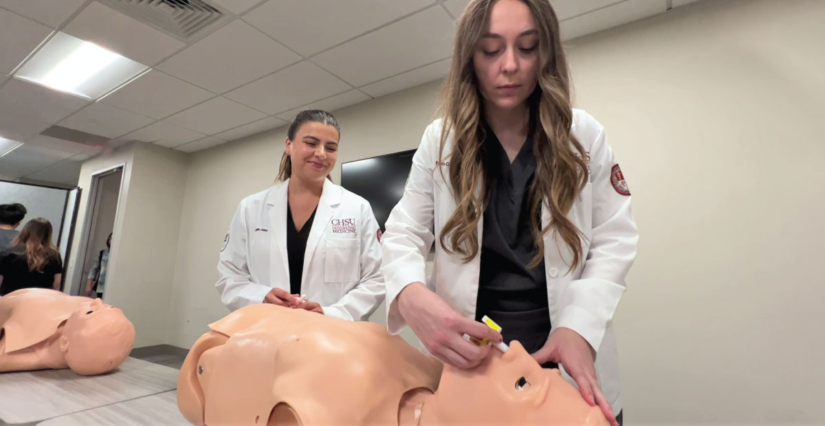 Women administer nasal spray to manikin trainer