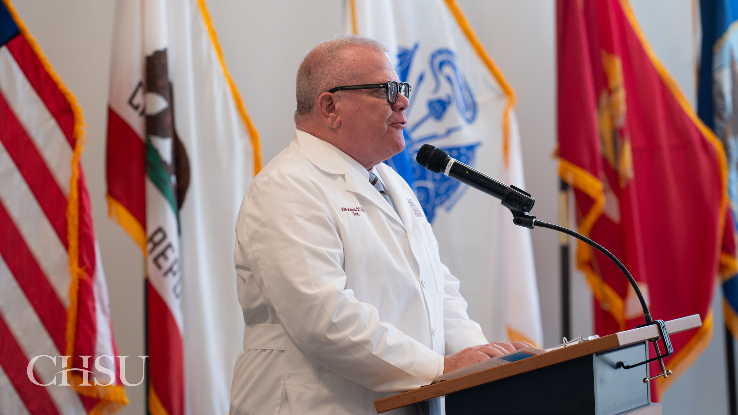 Dr Graneto speaking at podium with military and US flags in background
