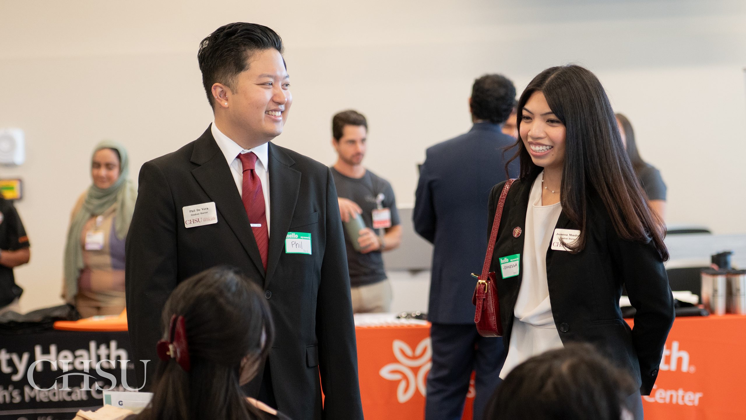 Two CHSU medical students in professional attire, smiling while networking with a seated representative at the CHSU 2026 Residency Fair.

