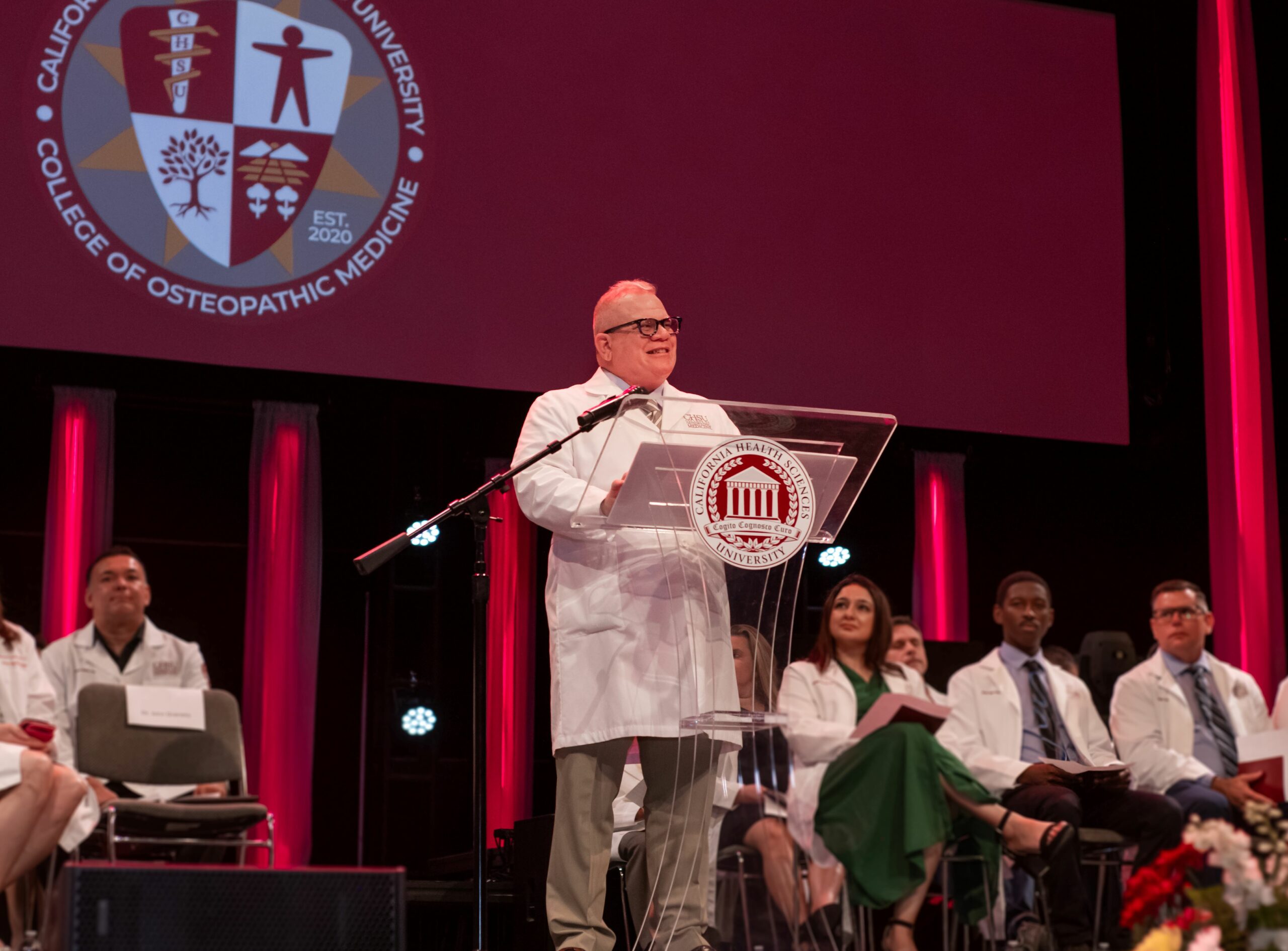 dean in white coat standing at podium