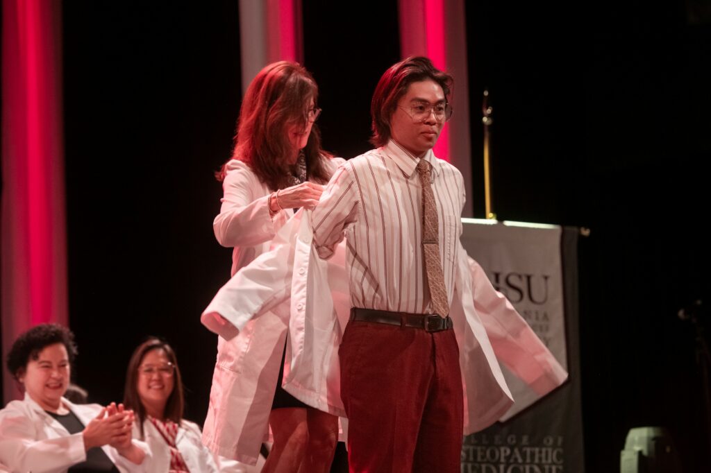 woman placing white coat onto male student