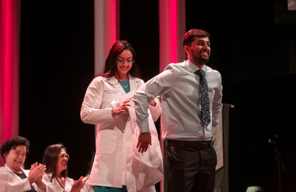 woman placing white coat on male student