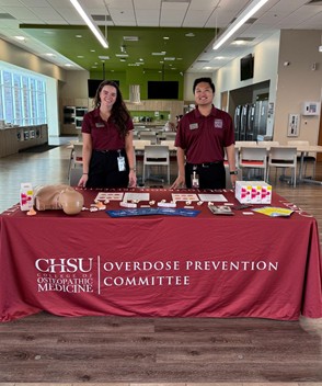 2 people behind table with manikin and overdose prevention supplies