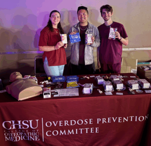 students standing behind table with manikin holding overdose prevention resources
