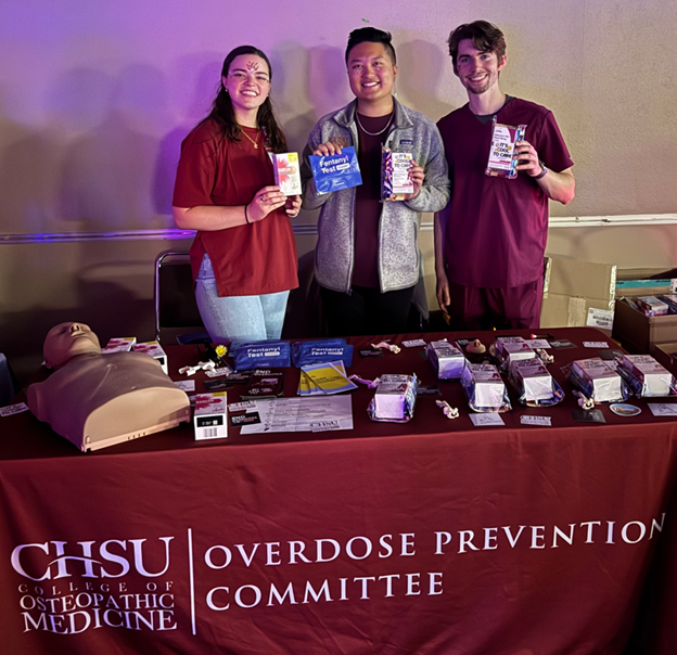 students standing behind table with manikin holding overdose prevention resources