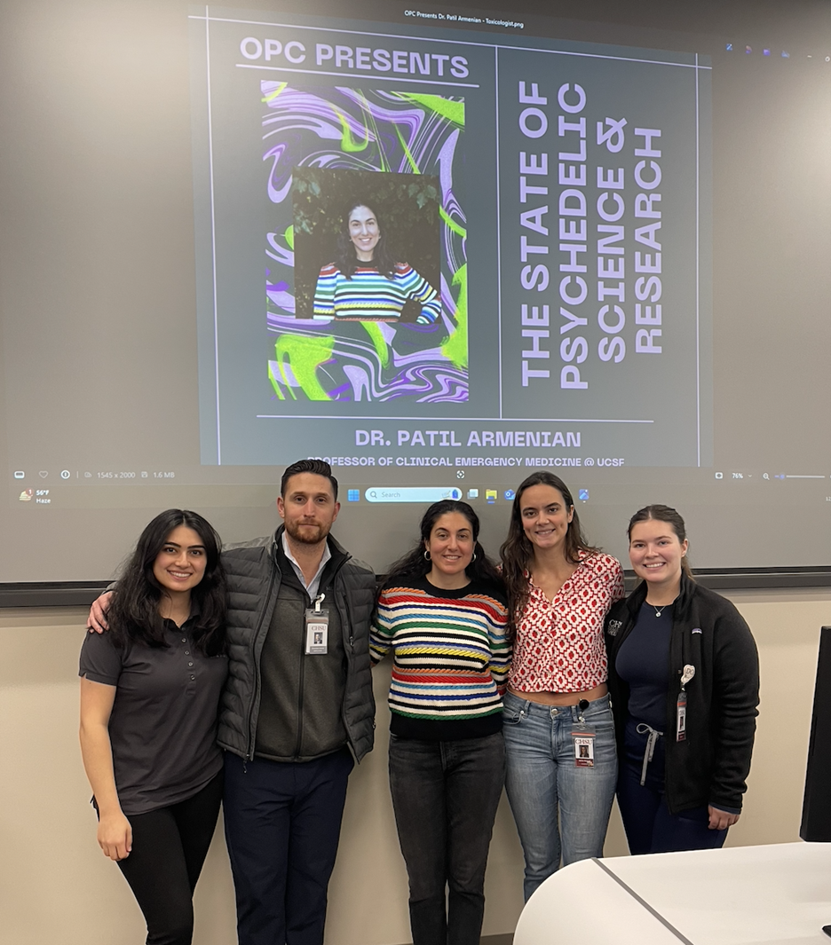 Five people taking group photo in front of screen in classroom