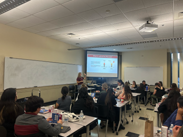 student presenting with screen in front of seated students in room