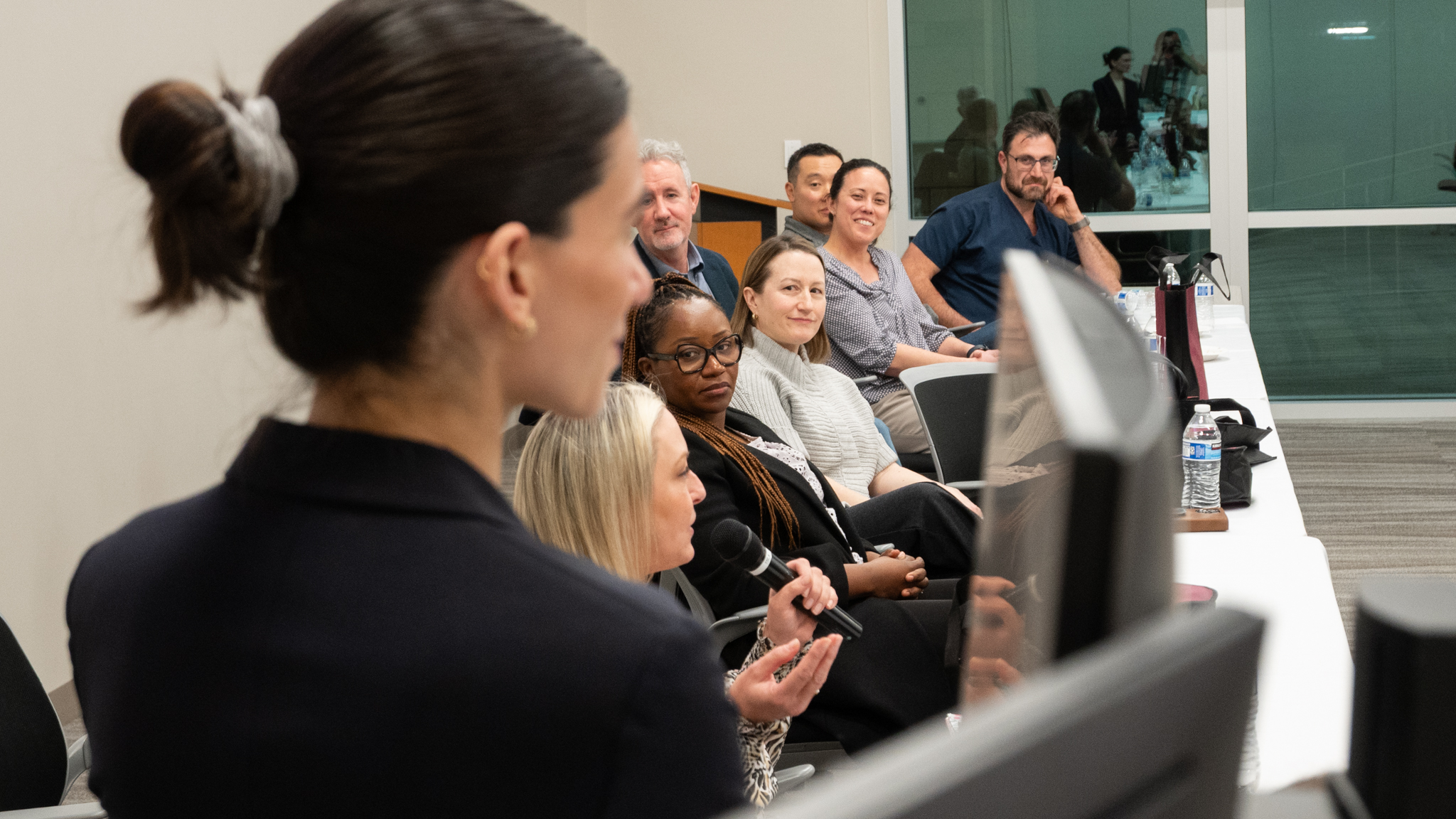 Photo of surgeons at panel table with person speaking holding microphone
