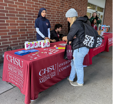 medical students at Overdose Prevention Committee table with supplies talking to student with backpack