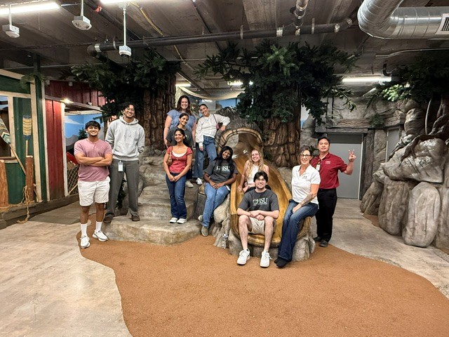 Eight first-year California Health Sciences University medical students, two CHSU admissions staff members, and one Fresno Mission staff member pose in a tree-themed children’s area at Fresno Mission.