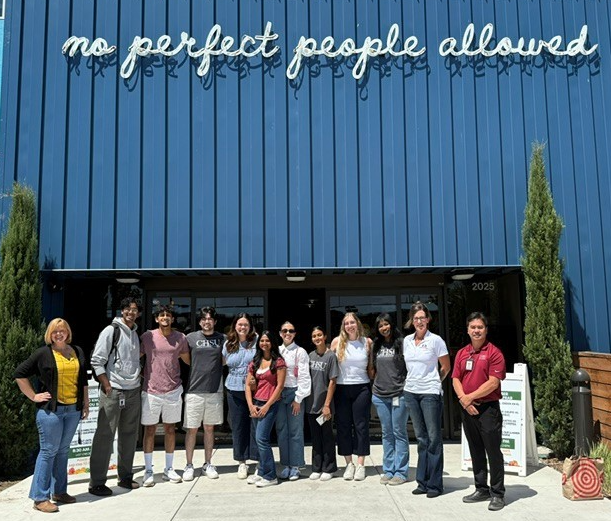California Health Sciences University first-year medical students, CHSU staff, and Fresno Mission staff pose outside Fresno Mission beneath a sign reading, “No perfect people allowed.”