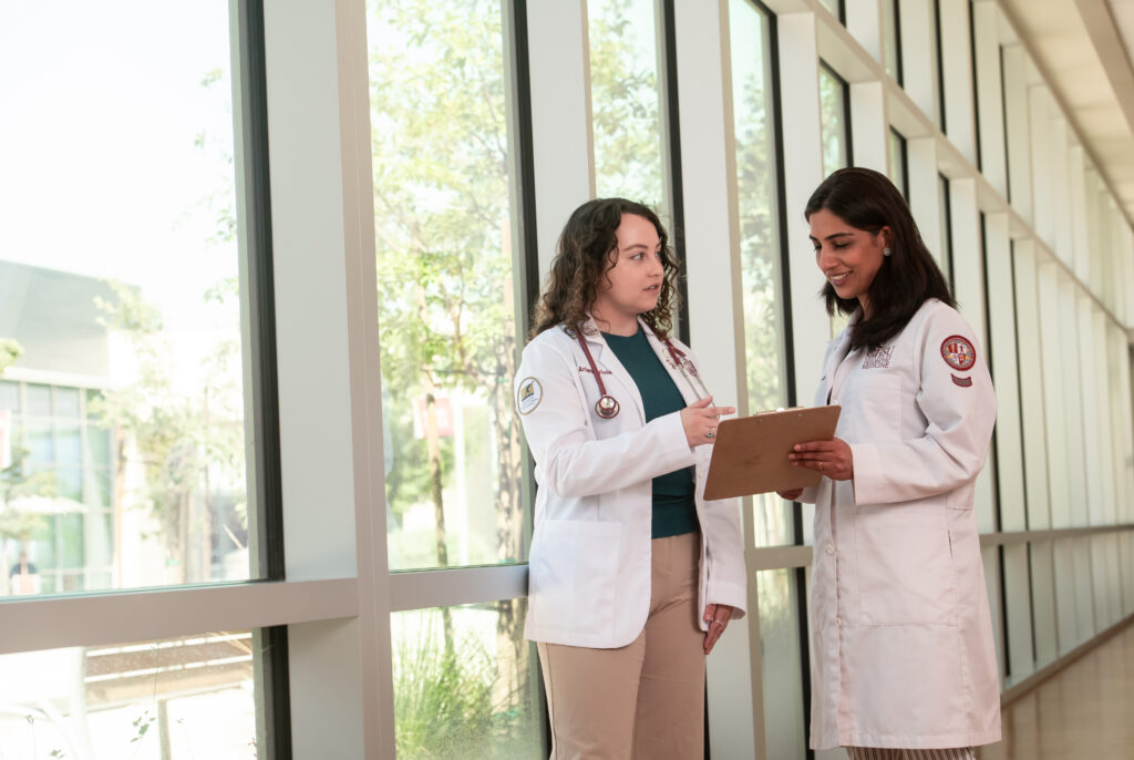 People in white coats looking at clipboard in hallway