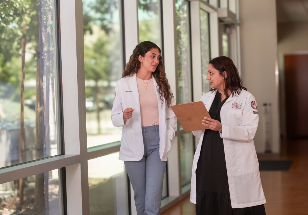 physician with clipboard walking in hallway with medical student