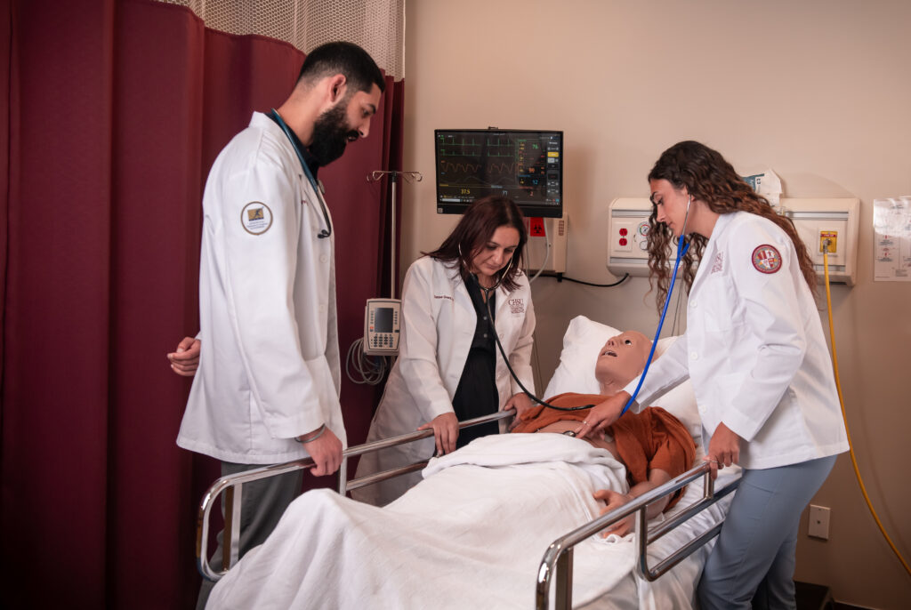 People in white coats working on manikin patient in hospital bed