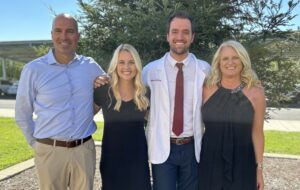 student in white coat with parents and wife