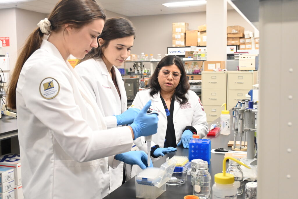 students and faculty in white coats conducting research in lab