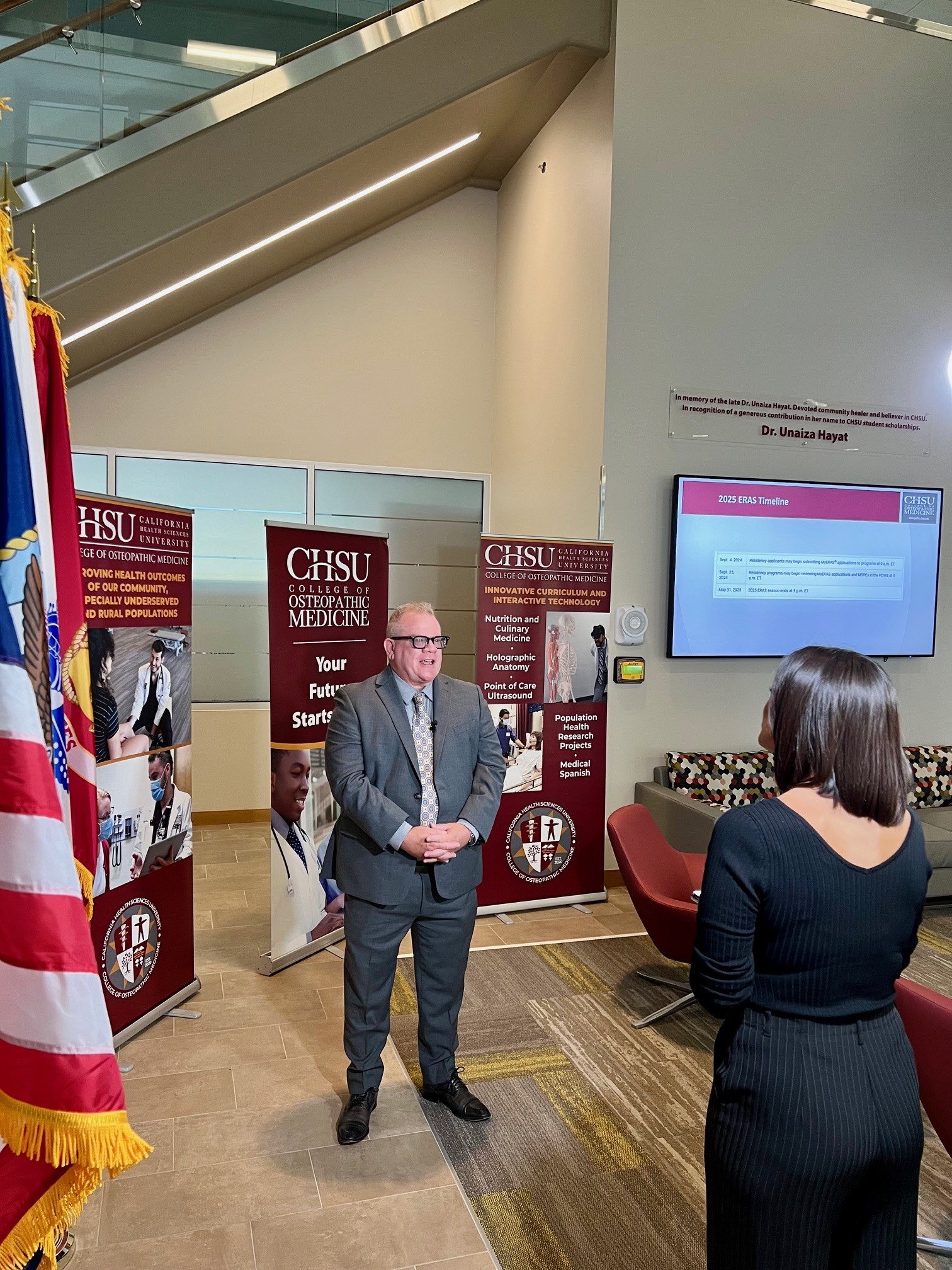 female reporter interviewing male dean of college with American flag in foreground