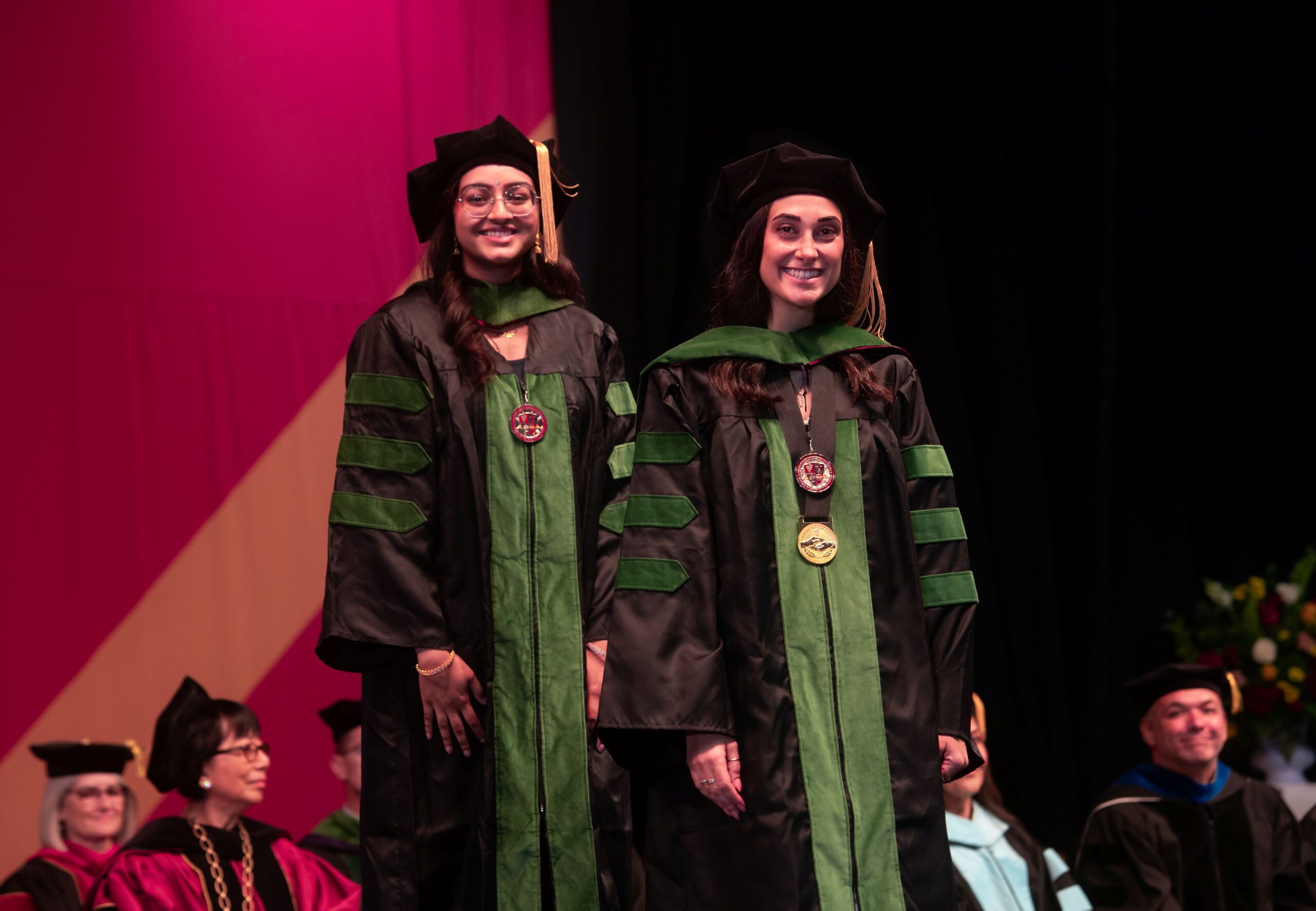 Dr Varsha Swamy and Dr. Tatiana Abdulnour standing on stage wearing academic regalia