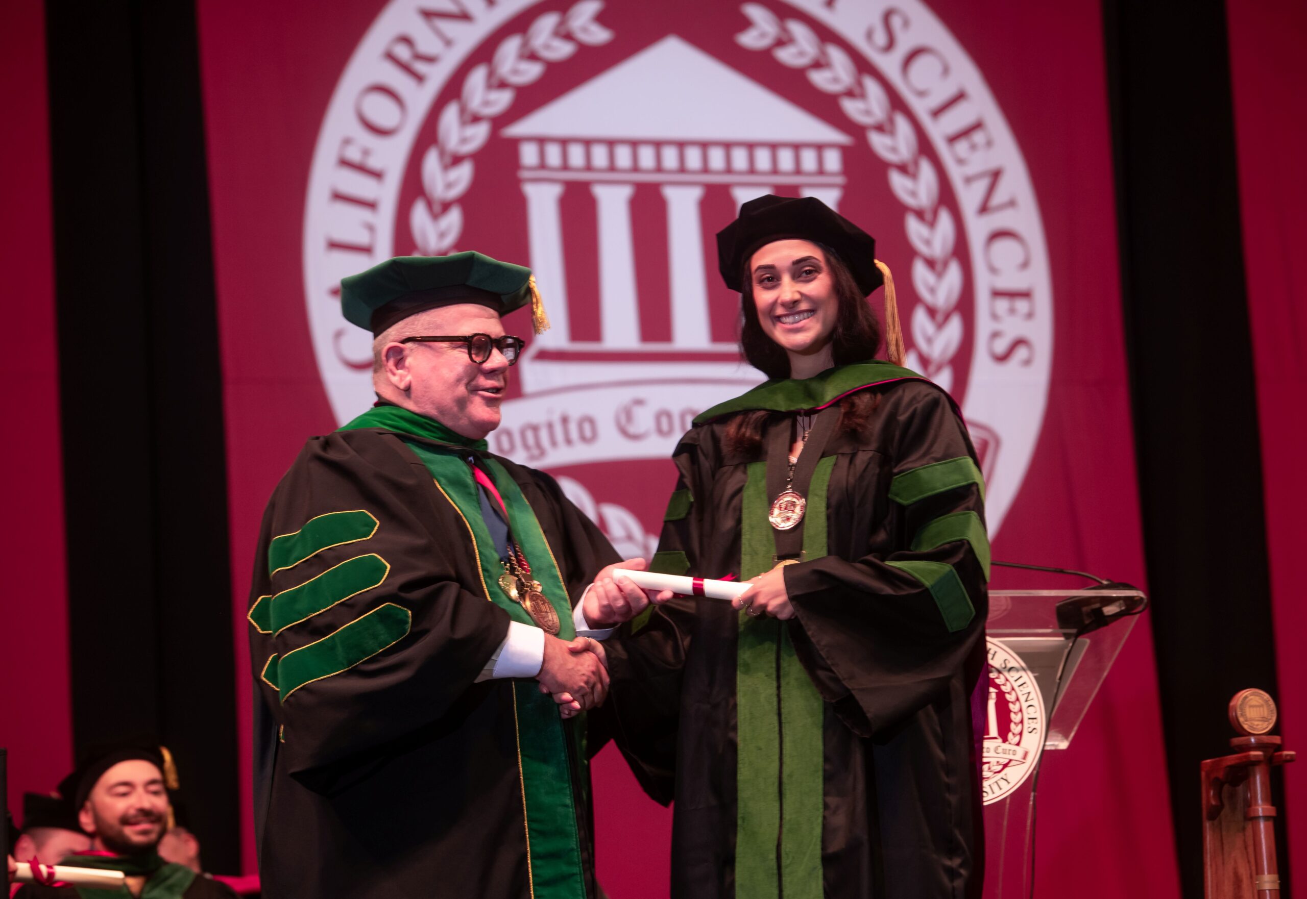 Dr Graneto handing diploma to graduate on stage at Commencement