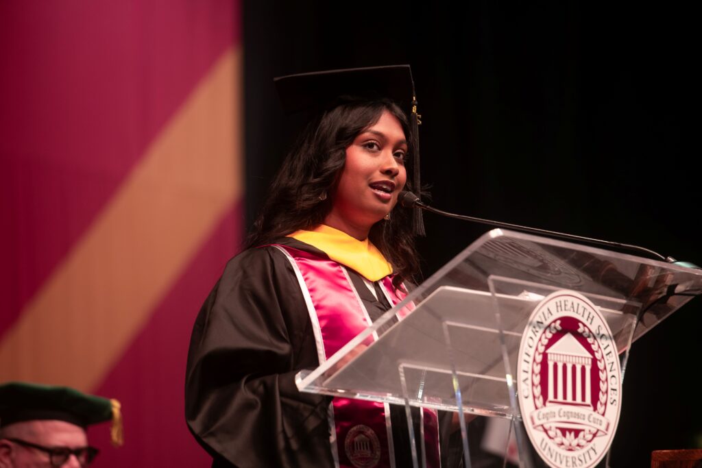 Roussolini Socrates speaking at podium in academic regalia