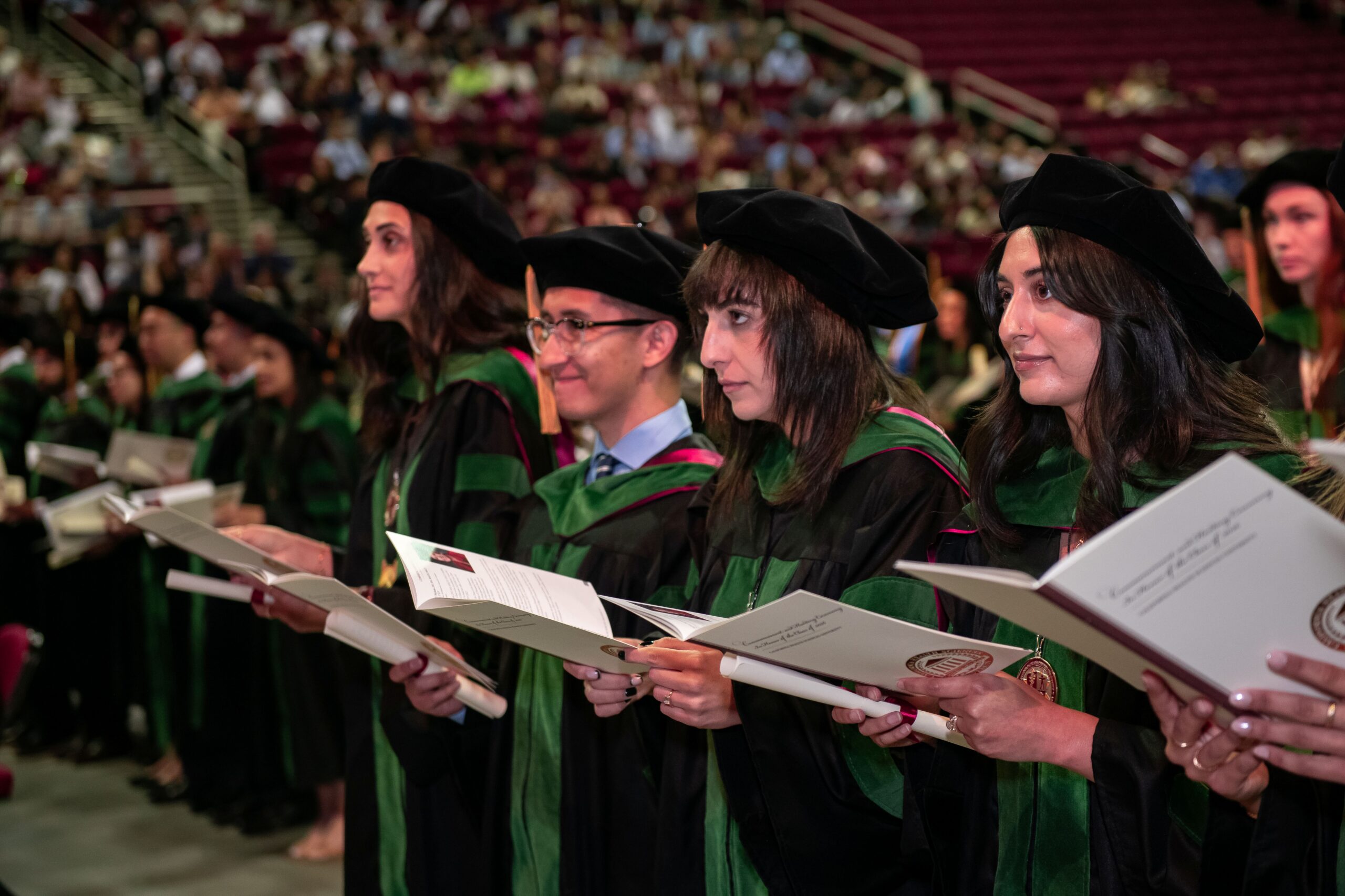 graduates standing and reading Osteopathic Oath wearing regalia at Commencement