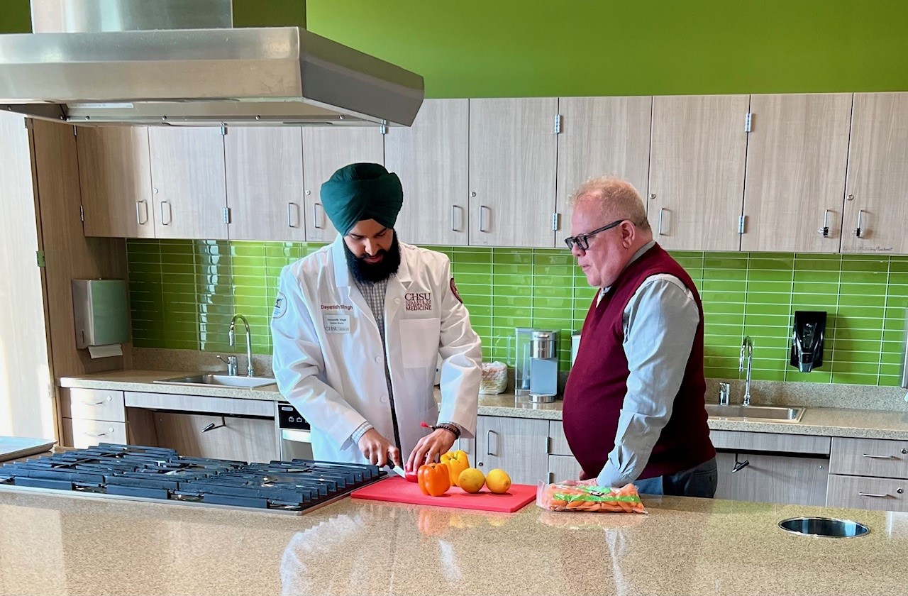 student chopping vegetables in kitchen with dean oversight