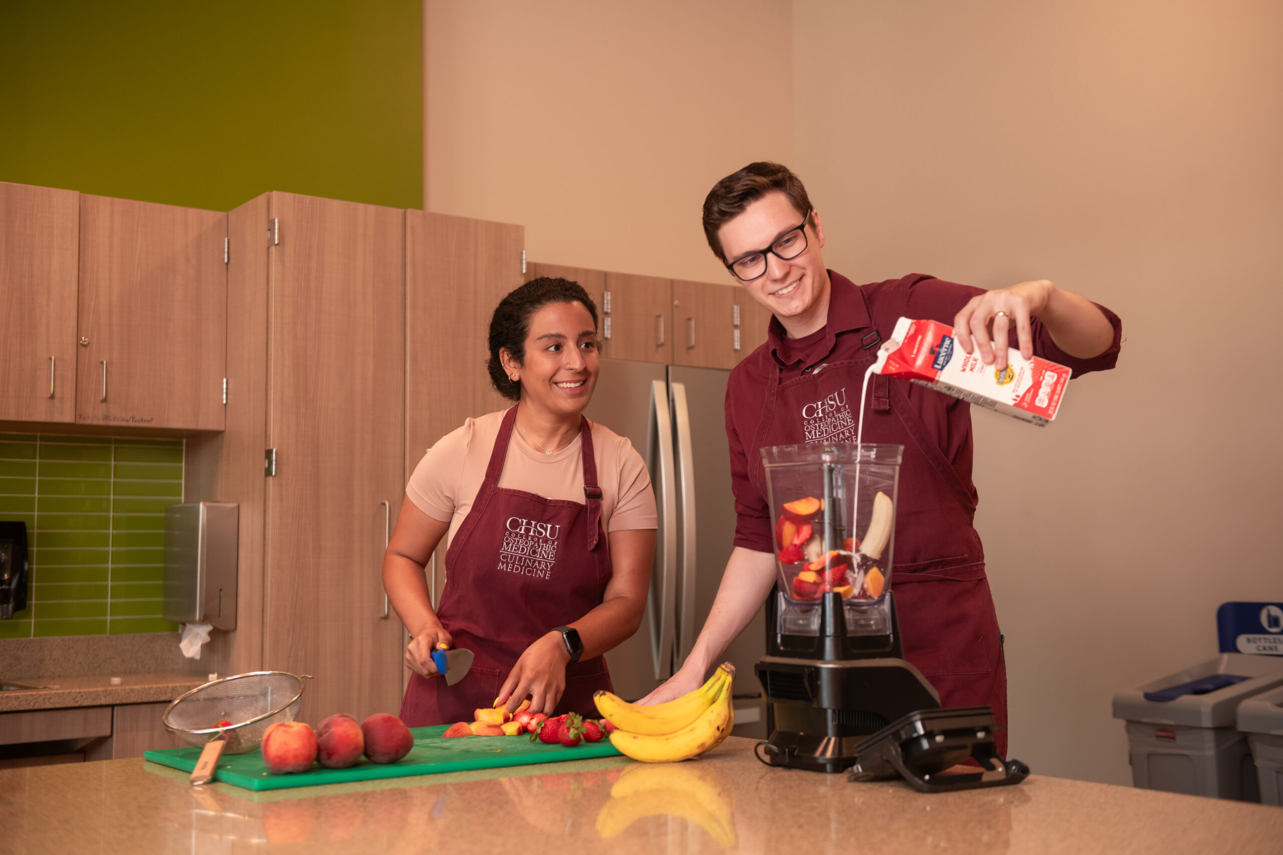 two students making smoothies in blender wearing aprons