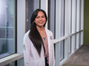 student in white coat standing by windows