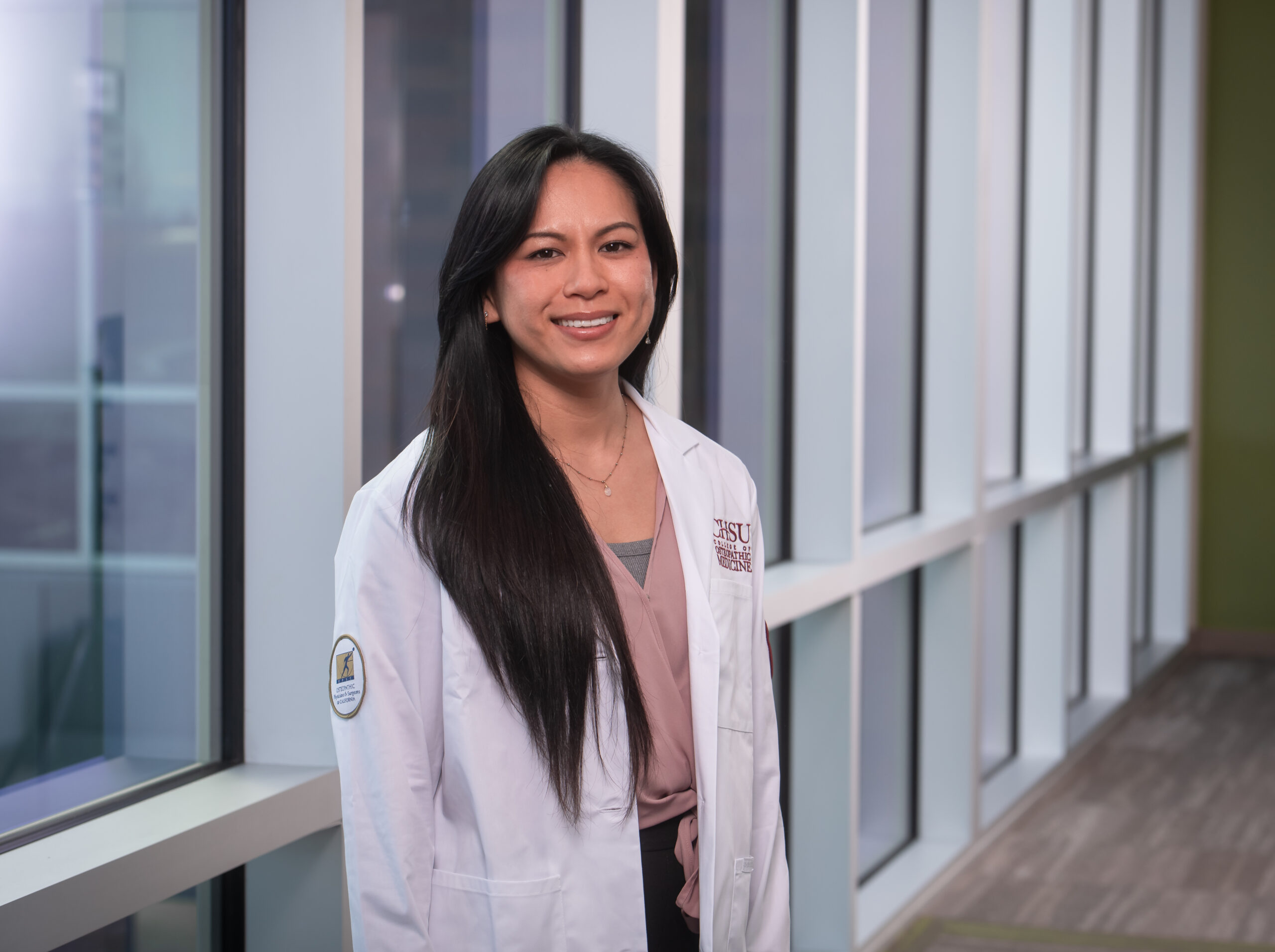 student in white coat standing by windows