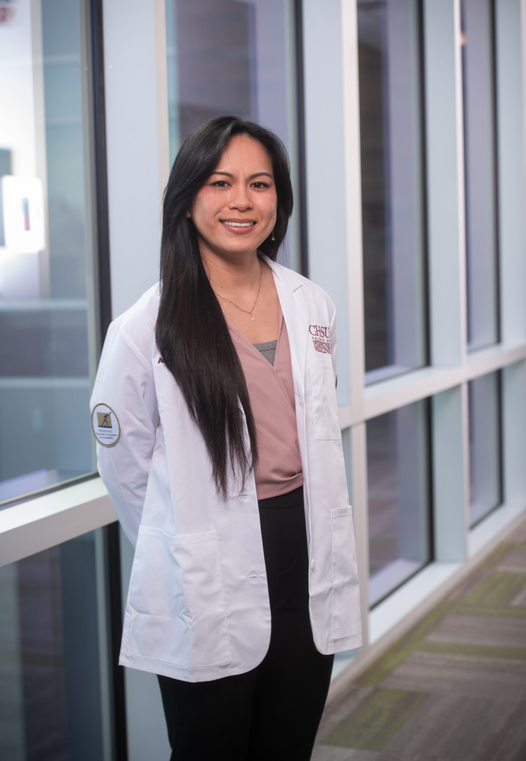 student in white coat standing by windows