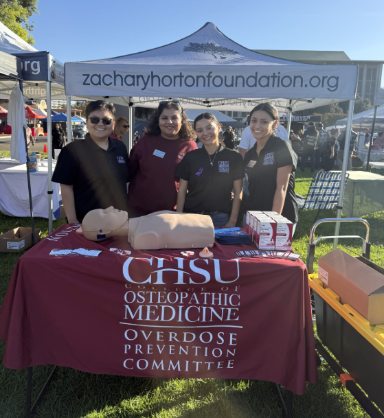 Four CHSU Overdose Prevention Committee members stand behind an outreach table with opioid overdose response training materials at SoberStock Fest.