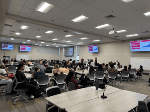 students at desk in classroom with presenters and presentation on screens