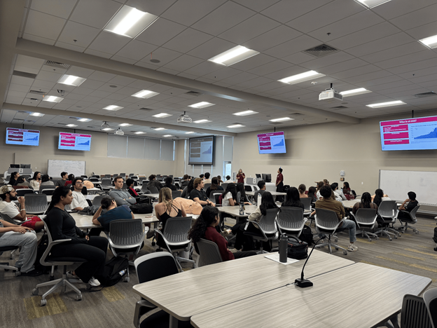 students at desk in classroom with presenters and presentation on screens
