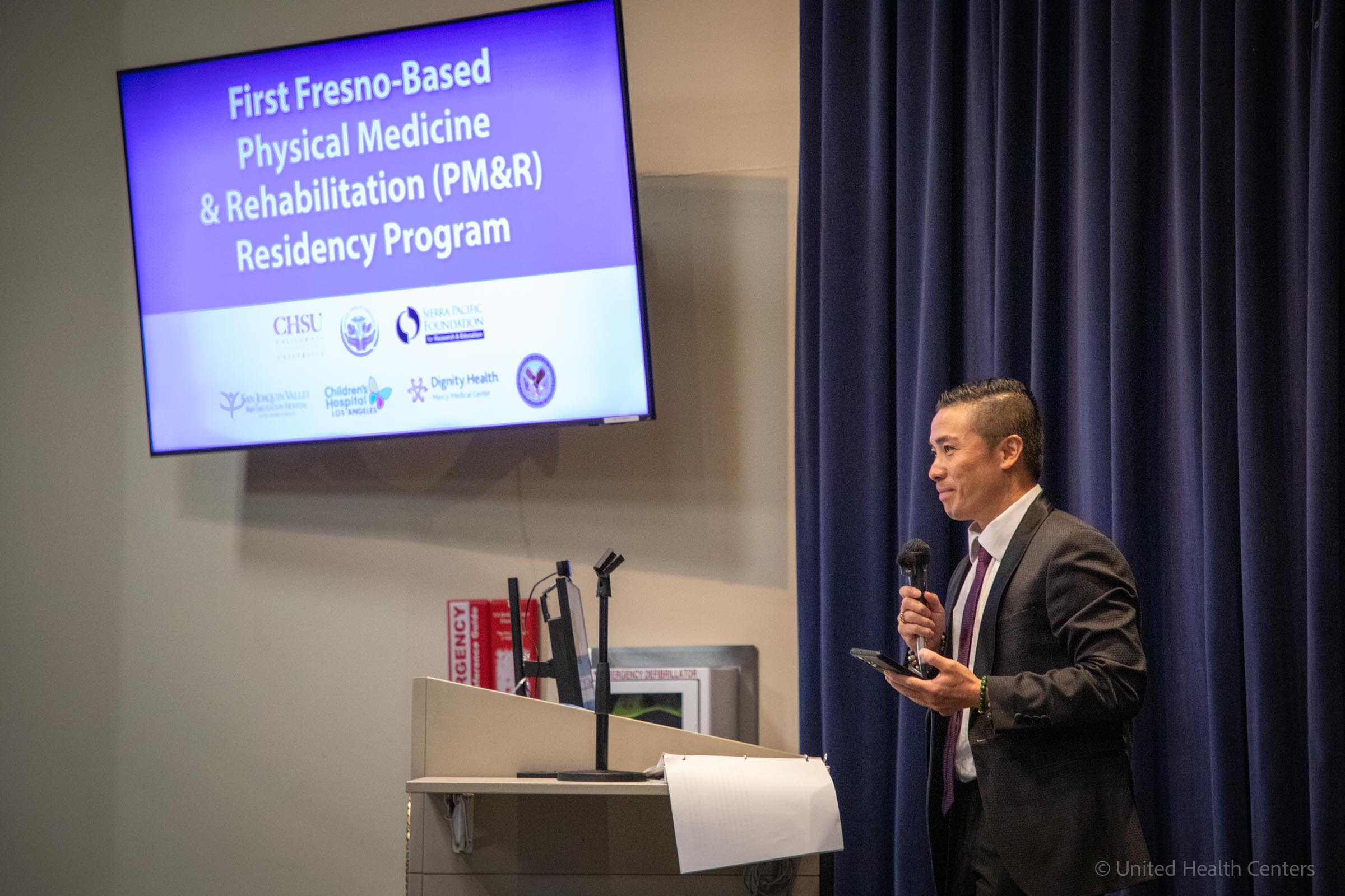 Dr. Duc Chung speaking at podium with screen in auditorium