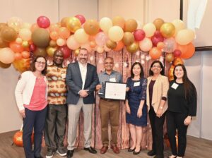 physician holding certificate with group in front of balloons