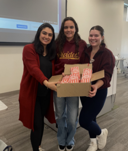 three people holding box of popcorn in front of screen