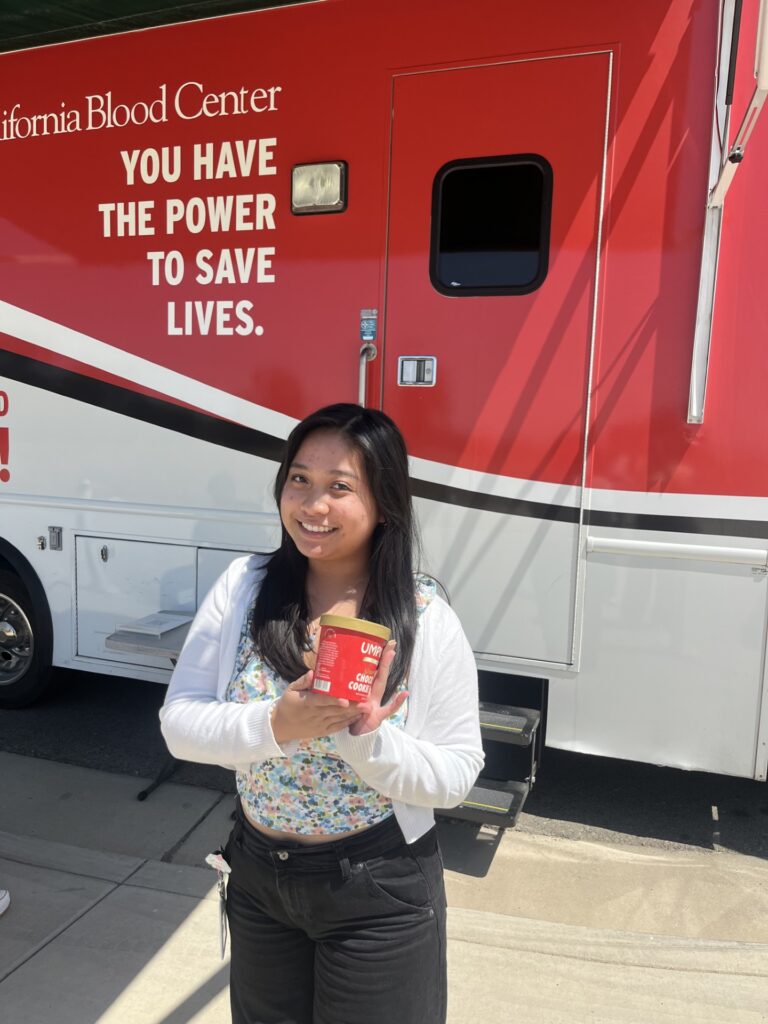 A CHSU Valley Reach medical student holds a pint of ice cream in front of the Central California Blood Center mobile donation unit during the blood drive at CHSU-COM.