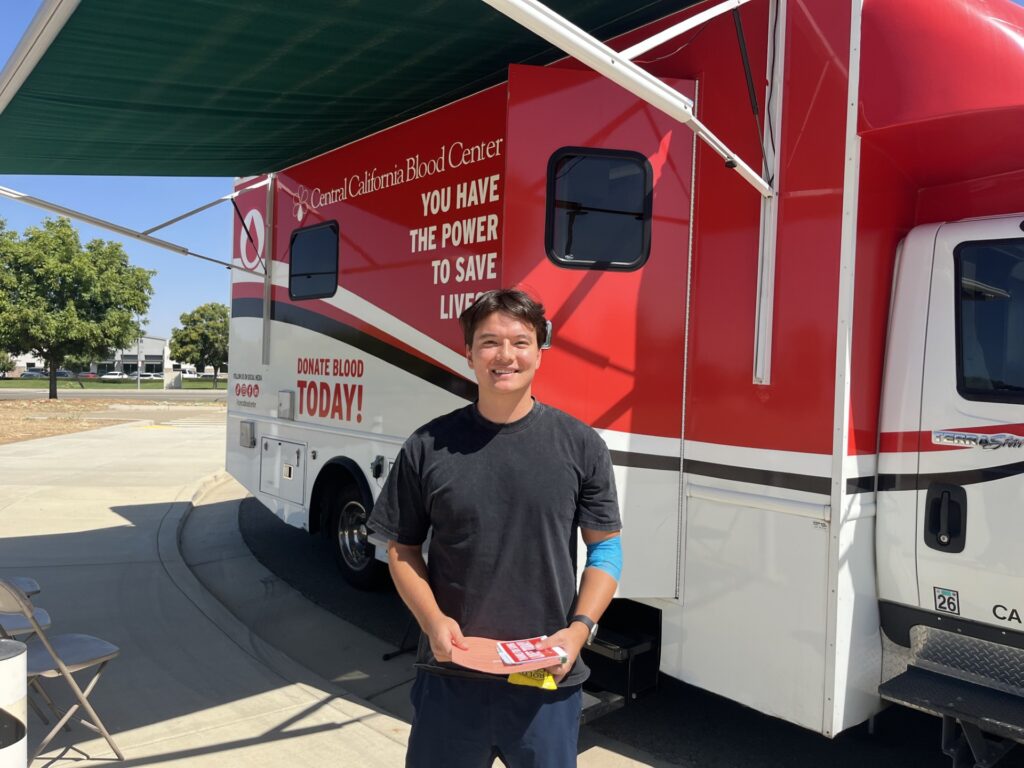 A CHSU Valley Reach medical student stands in front of a Central California Blood Center mobile donation unit during the blood drive at CHSU-COM.