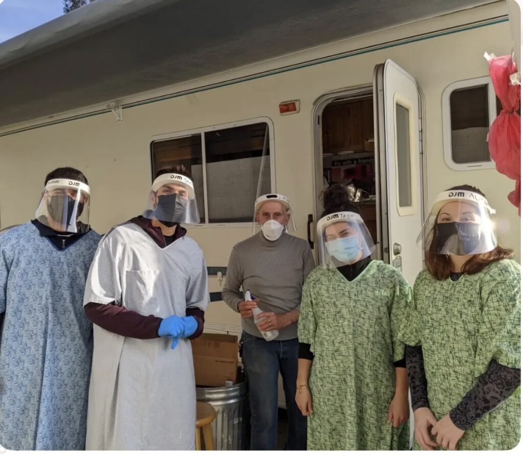 Two CHSU Valley Reach medical students and three San Joaquin Valley Free Medical Clinic and Needle Exchange staff members wear masks, face shields, and protective gowns outside a mobile clinic.