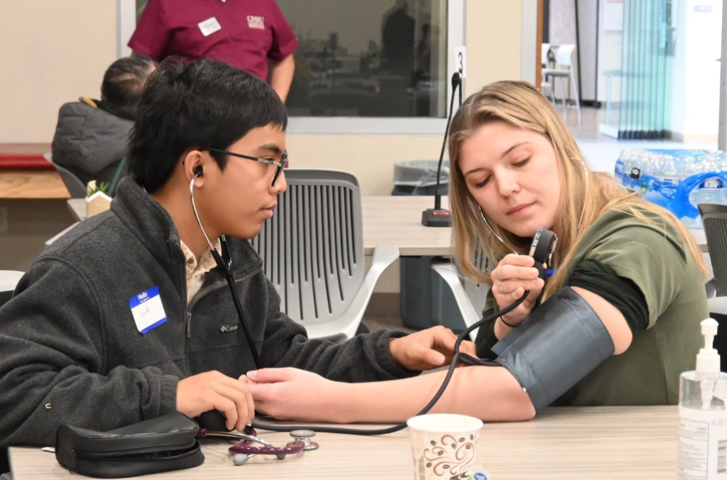 student using Sphygmomanometer to take manual blood pressure of another student wearing cuff on arm