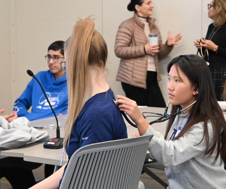 student holding stethoscope on back of another student 